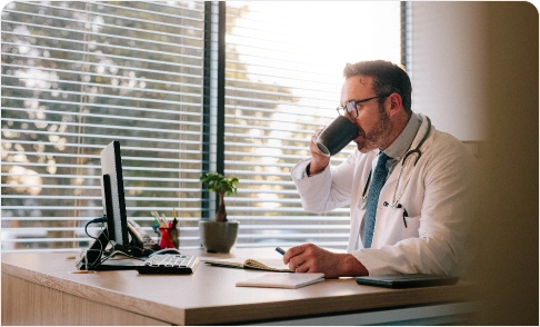 Doctor in front of a computer drinking coffee